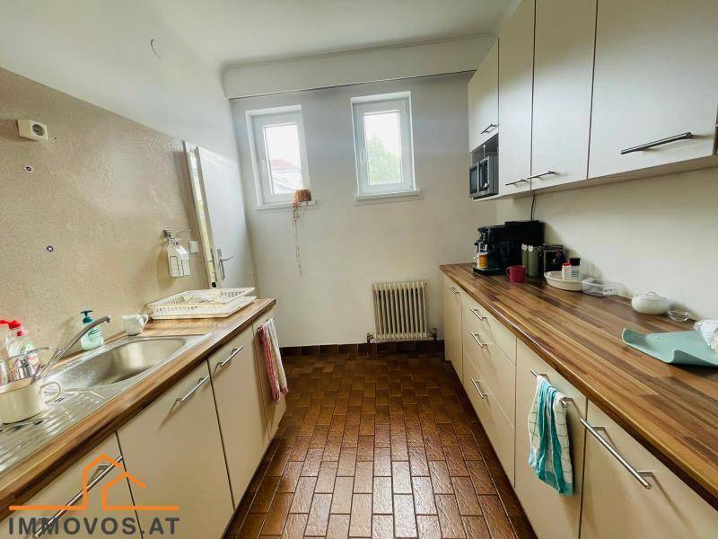 Funktionale Teeküche mit Holz-Arbeitsplatten, Einbauschränken und zwei Fenstern für Tageslicht.