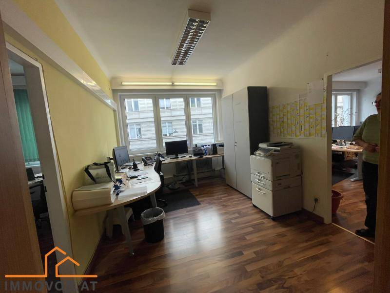 Büro mit mehreren Arbeitsplätzen, großen Fenstern und gelben Wänden, die eine freundliche Atmosphäre schaffen.