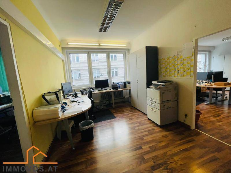 Geräumiges Büro mit mehreren Arbeitsplätzen, großen Fenstern und gelben Wänden für eine helle Umgebung.