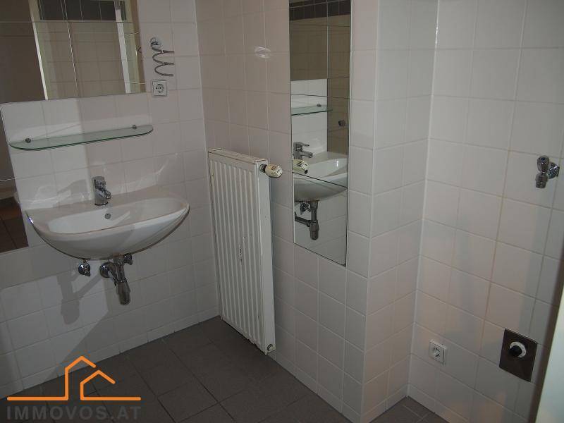 Helles Badezimmer mit Waschbecken, Heizkörper und weißen Wandfliesen.