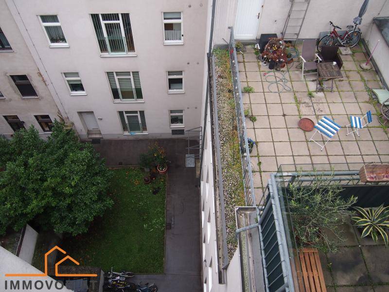 Blick von oben auf eine gepflasterte Terrasse mit Sitzgelegenheiten und einem kleinen Gartenbereich.