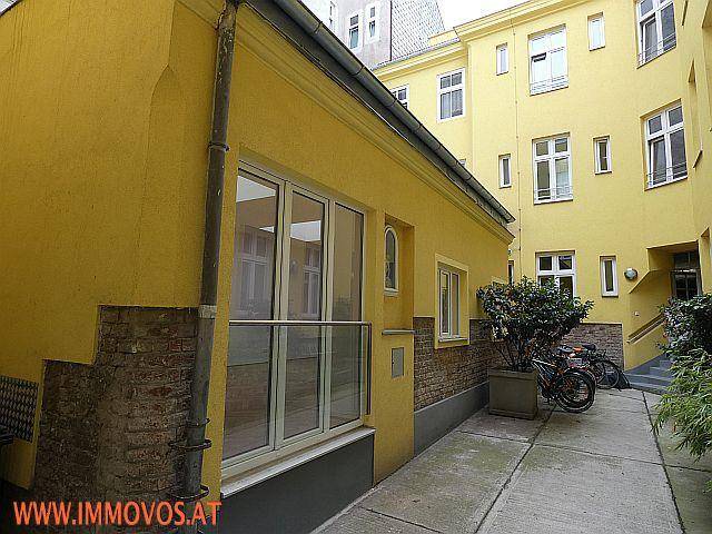 Gelbe Gebäudefassade in einem Innenhof mit Fenstern, einem kleinen Balkon und Fahrrädern.