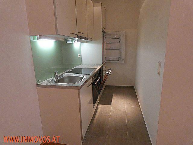 Kompakte, moderne Küchenzeile mit weißen Schränken, Spüle und integrierten Elektrogeräten in schmalem Raum.