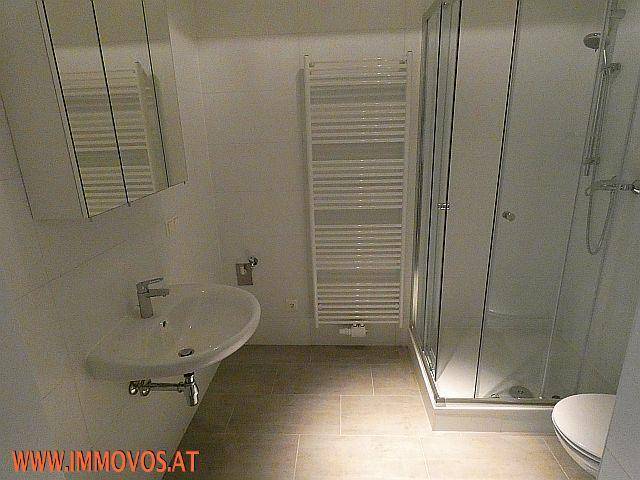 Modernes Badezimmer mit Duschkabine, Waschbecken, Handtuchheizkörper und hellen Fliesen.