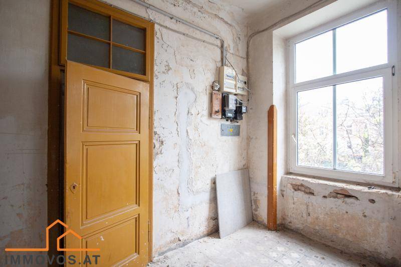 Renovierungsbedürftiger Raum mit alter Holztür, Fenster und sichtbaren Elektroinstallationen.