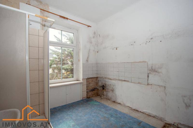Badezimmer in sanierungsbedürftigem Zustand mit Duschkabine, Fliesen und einem Fenster.