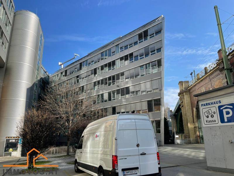 Moderne Bürogebäude-Fassade mit markanter Architektur und großen Fenstern, davor ein Lieferwagen und eine Brücke.