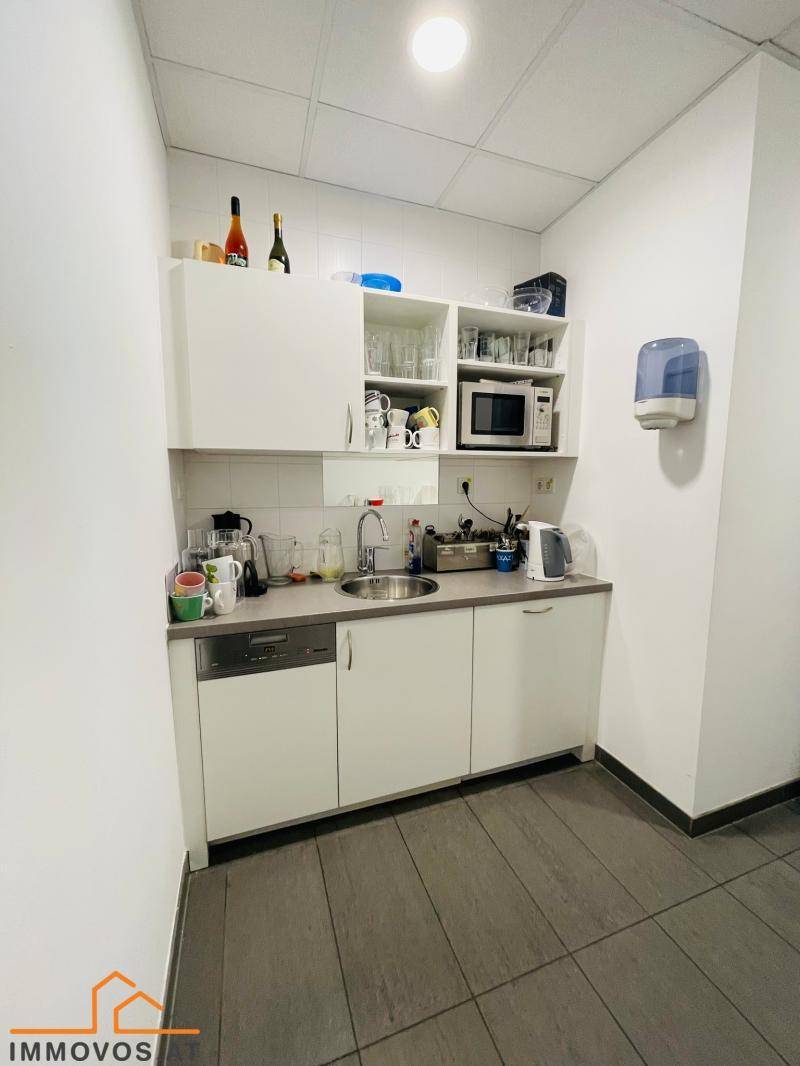 Kleine, funktionale Küchenzeile mit weißen Schränken, Spüle, Mikrowelle und Geschirrspüler in einem Bürobereich.