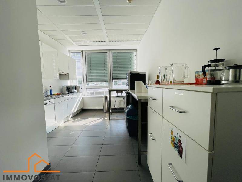 Helle Küchenzeile mit weißen Schränken, Arbeitsplatte, Spüle und Fenster, ideal für Pausen im Büro.