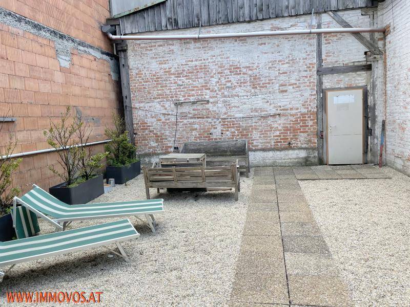 Rustikale Terrasse mit Kiesboden, Liegestühlen und einer alten Ziegelwand im Hintergrund.