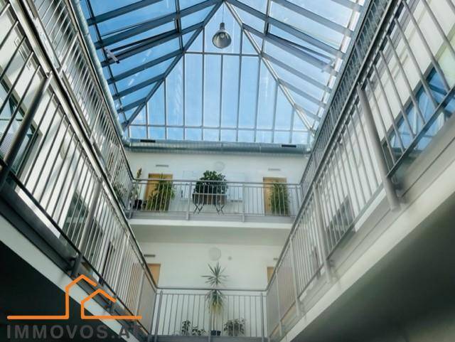 Helles Atrium mit Glasdach, das viel Tageslicht spendet, und umlaufenden Galerien.