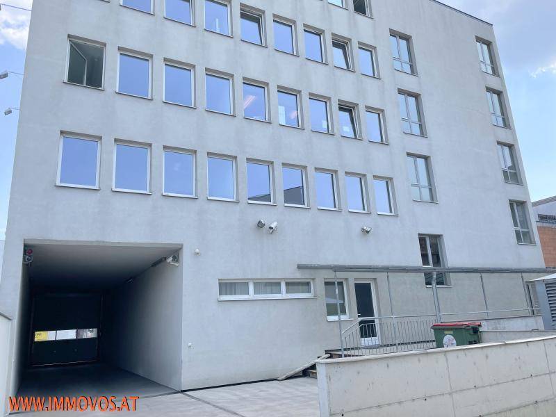 Mehrstöckiges Gebäude mit vielen Fenstern und einer Einfahrt zu einer Tiefgarage.