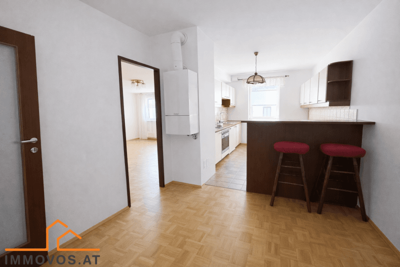 Funktionale Küche mit weißen Schränken, Frühstücksbar und Blick in einen weiteren Raum.