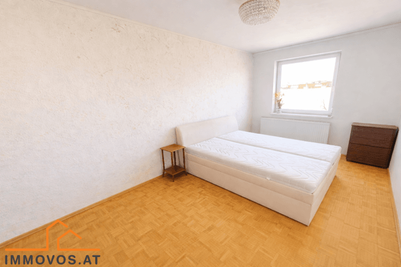 Schlafzimmer mit Parkettboden, Doppelbett und einem Fenster, das für natürliches Licht sorgt.