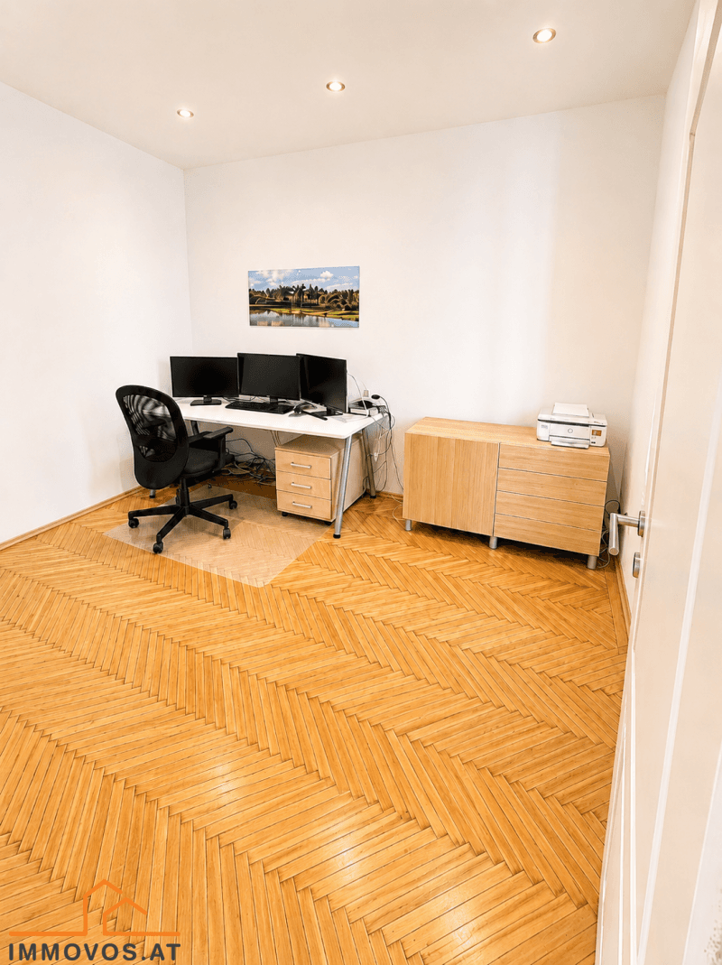 Funktionales Büro mit Fischgrätparkett, Schreibtisch mit mehreren Monitoren und Holzschrank.