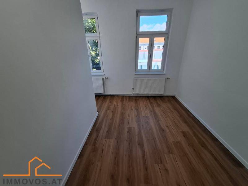 Heller Raum mit Laminatboden und zwei Fenstern, die einen Blick auf die Umgebung ermöglichen.