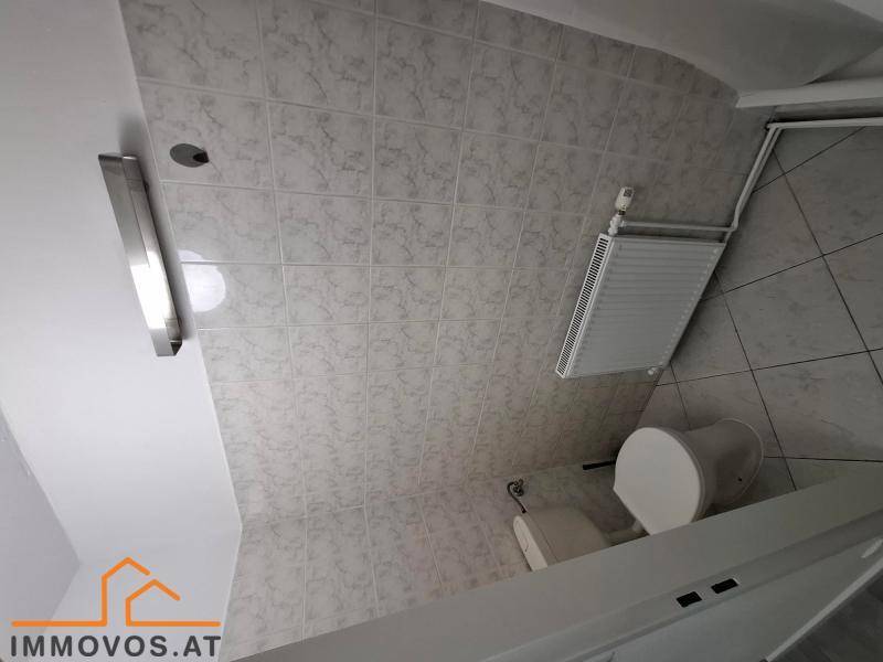 Badezimmer mit hellen Fliesen an Wänden und Boden, ausgestattet mit Toilette und Heizkörper.