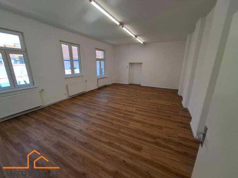 Geräumiger, heller Raum mit Laminatboden, weißen Wänden und Deckenleuchten, ideal für verschiedene Nutzungen.