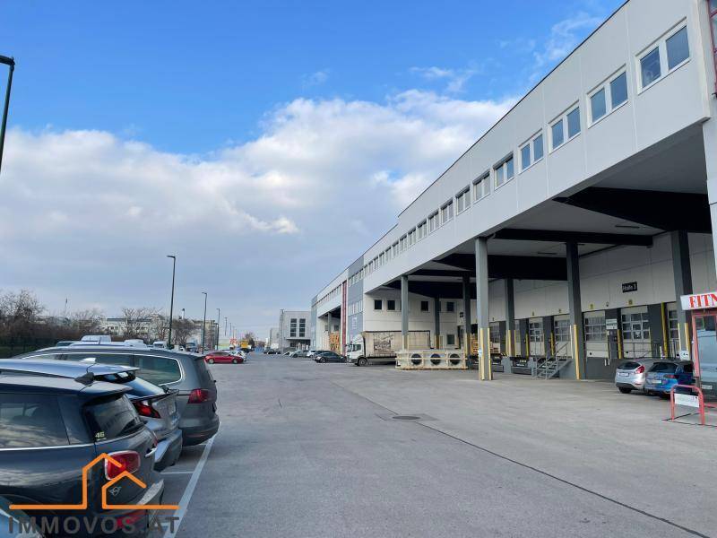 Großes Industriegebäude mit mehreren Laderampen und weitläufigem Parkplatz unter blauem Himmel.