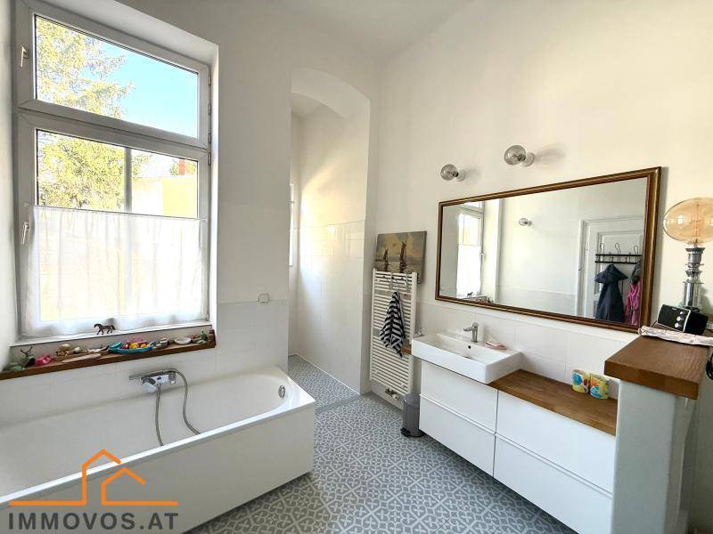 Helles Badezimmer mit Badewanne, Fenster und modernem Waschtisch, gut beleuchtet.