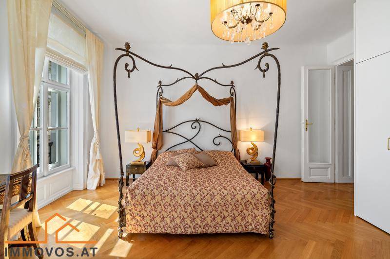 Helles Schlafzimmer mit schmiedeeisernem Himmelbett, Fischgrätparkett und hohen Fenstern.
