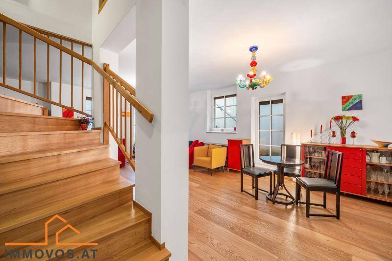Heller Eingangsbereich mit Holztreppe und offenem Übergang zum farbenfrohen Wohnzimmer.