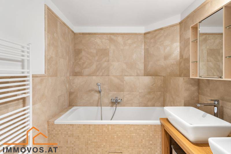 Badezimmer mit Badewanne, modernem Waschtisch und beigefarbenen Fliesen.