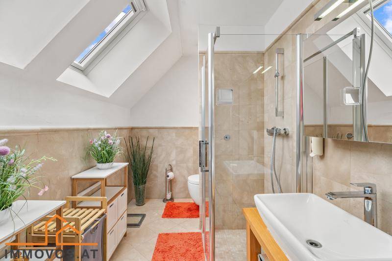 Modernes Badezimmer im Dachgeschoss mit Dusche, Waschtisch und Dachfenster für Tageslicht.