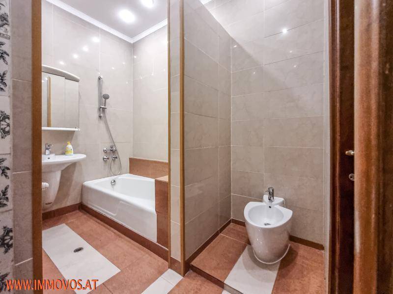 Badezimmer mit Badewanne, Bidet, Waschbecken und Fliesenboden in warmen Farbtönen.