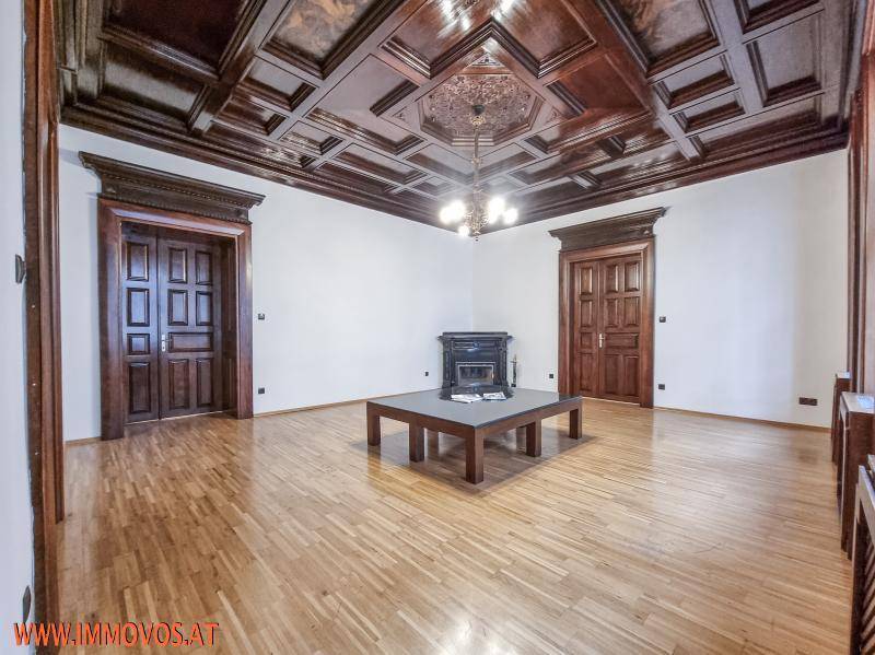 Eleganter Wohnraum mit dunkler Holzkassettendecke, Parkettboden und zentralem Kamin.