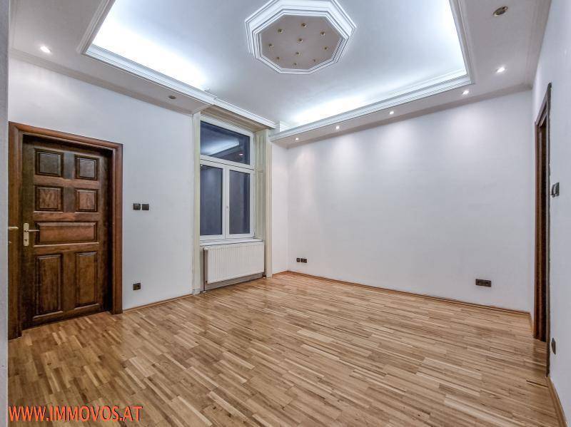 Helles Zimmer mit Parkettboden, Einbaudeckenleuchten und einem großen Fenster.