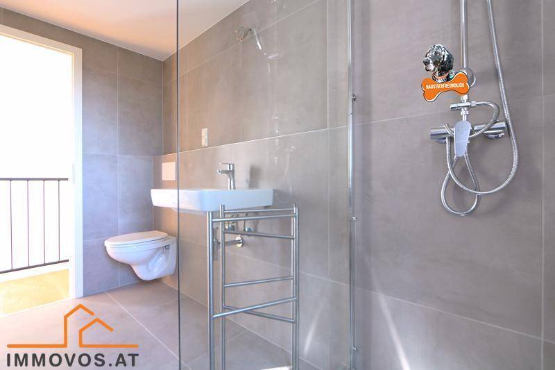 Zeitgemäßes Badezimmer mit grauen Fliesen, wandhängendem WC und Glasdusche.