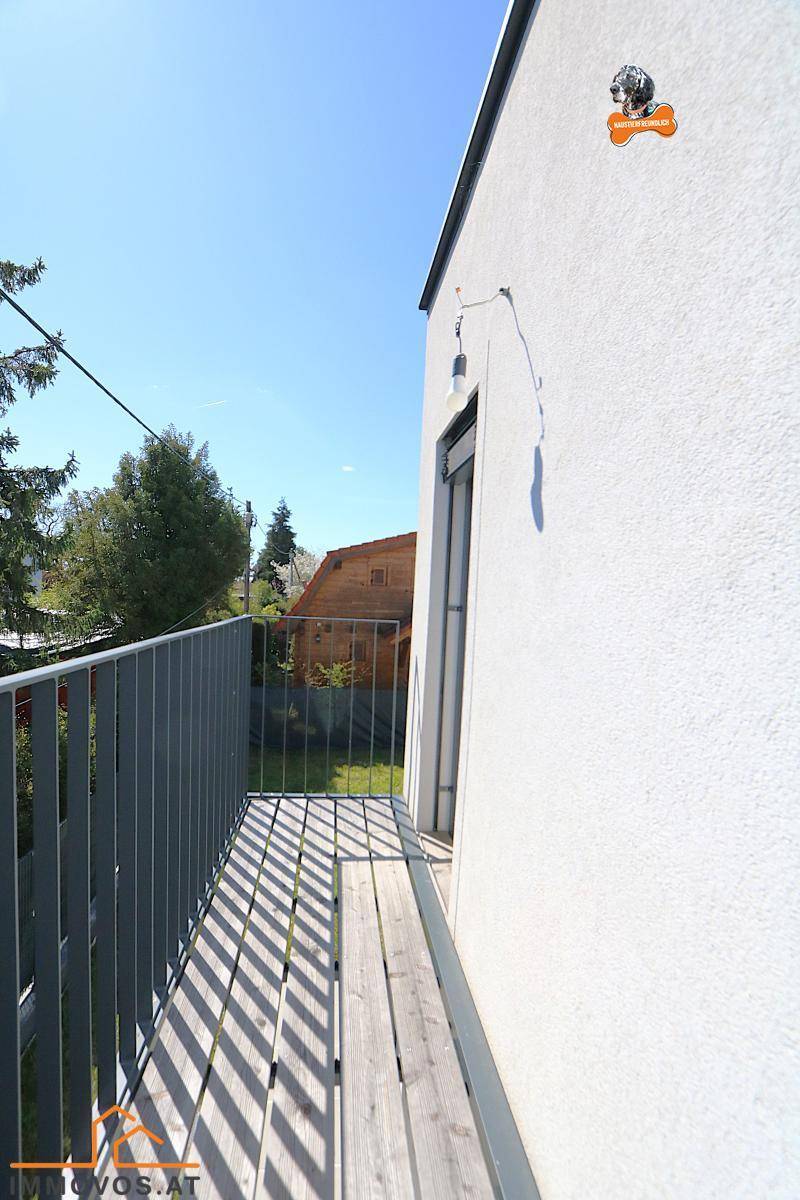Schmaler Balkon mit Metallgeländer und Holzboden, bietet Blick ins Grüne.