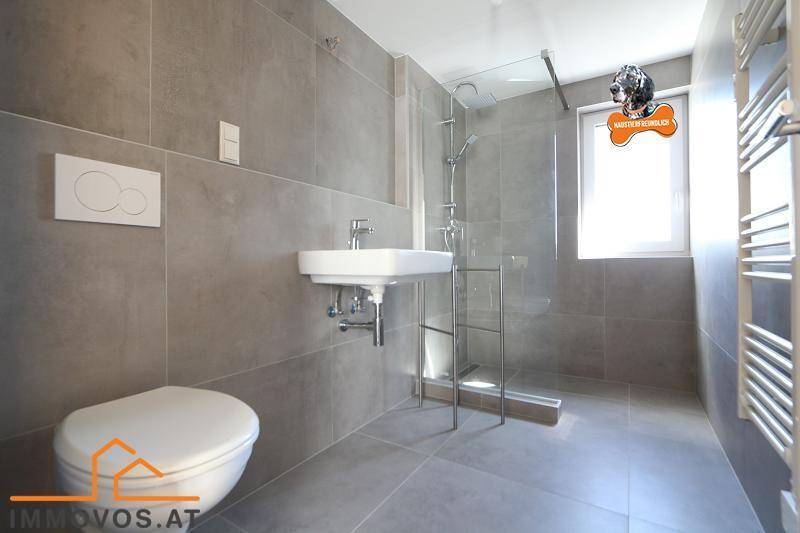 Modernes Badezimmer mit grauen Fliesen, wandhängendem WC und ebenerdiger Dusche.