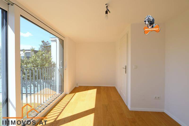 Lichtdurchflutetes Zimmer mit Holzboden und breiter Fensterfront zum Balkon.