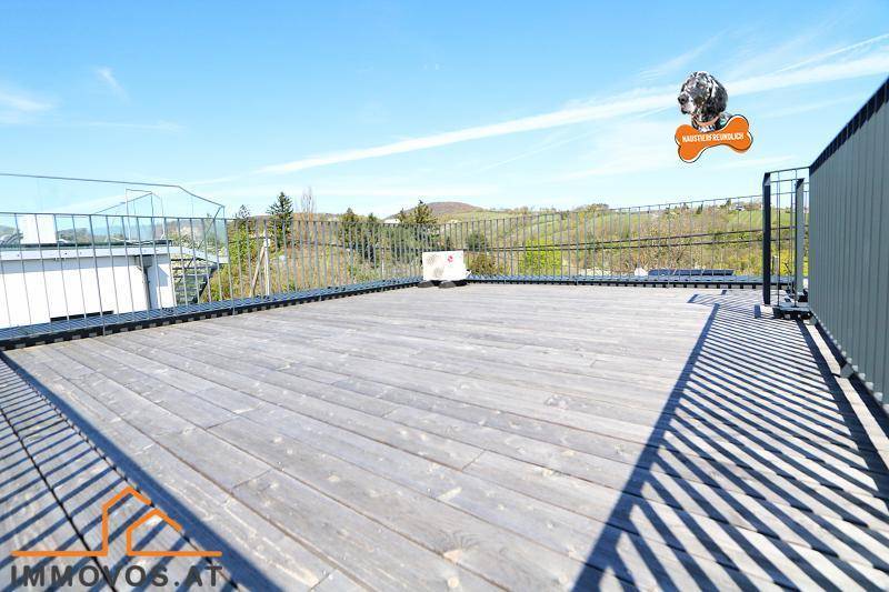 Weitläufige Dachterrasse mit Holzdielen und Panoramablick auf die grüne Umgebung.