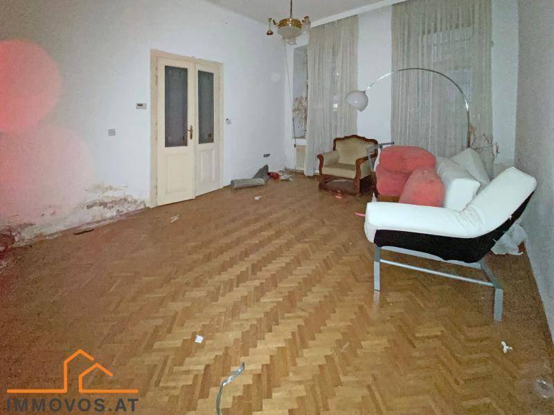 Geräumiges Wohnzimmer mit Fischgrätparkett und Renovierungsbedarf, zeigt Spuren der Zeit.