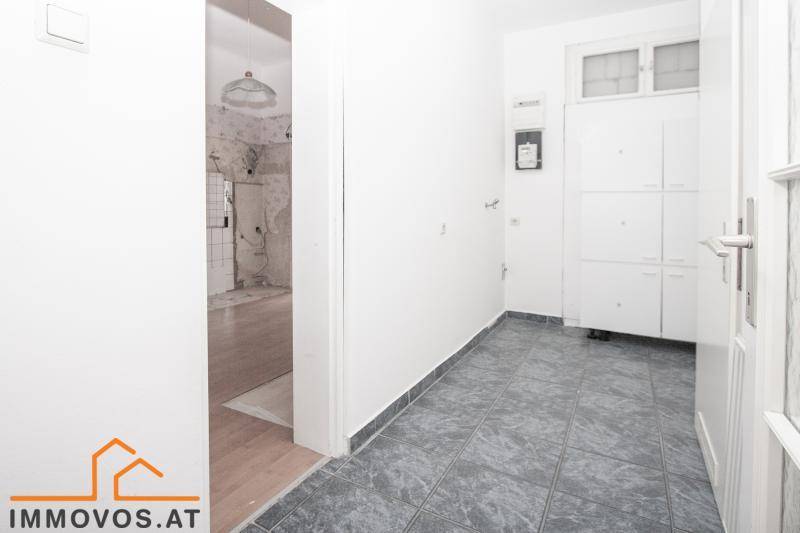 Heller Flur mit Fliesenboden und Blick in einen renovierungsbedürftigen Raum, mit Einbauschränken.