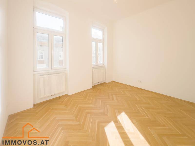 Ruhiges, leeres Schlafzimmer mit Fischgrätparkett und zwei Fenstern, ideal für erholsame Nächte.