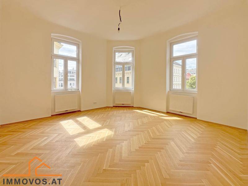 Geräumiges, leeres Zimmer mit Fischgrätparkett und drei großen Fenstern, die viel Licht hereinlassen.