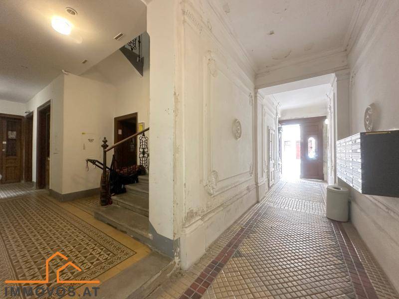 Historischer Eingangsbereich mit originalen Fliesen, Stuckelementen und Treppenaufgang in einem Altbau.