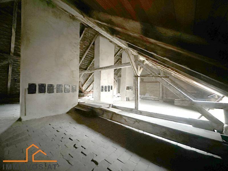 Weitläufiger Dachboden mit sichtbaren Holzkonstruktionen und alten Kaminzügen, wartet auf Renovierung.