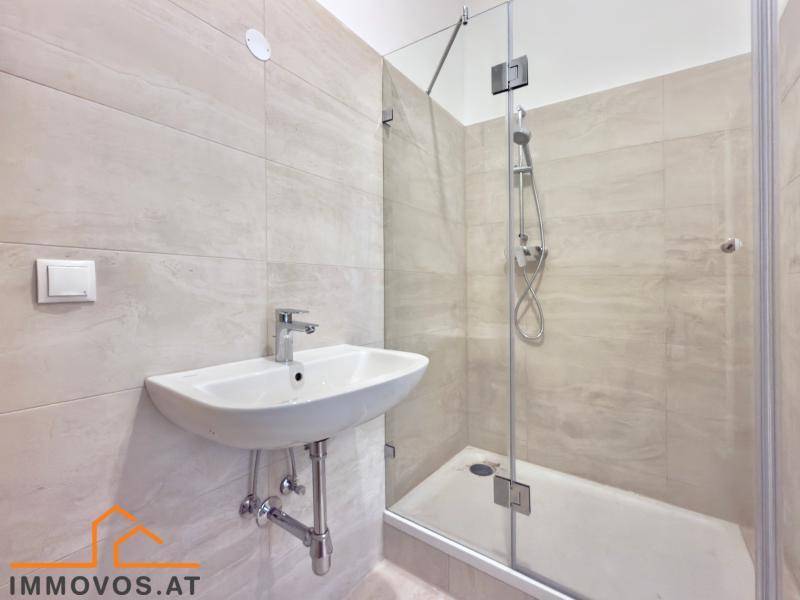 Modernes Badezimmer mit begehbarer Dusche, Waschbecken und hellen Fliesen.