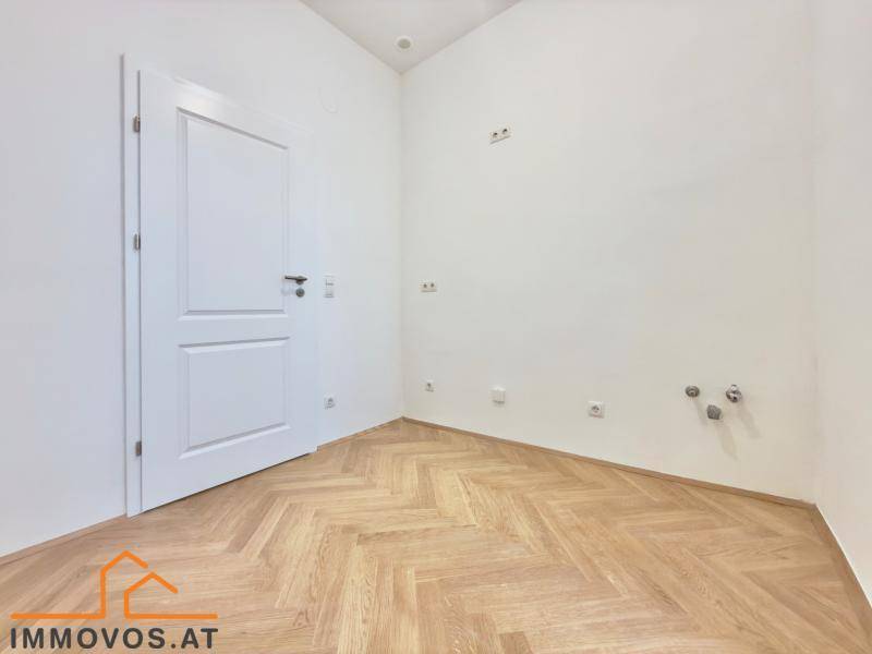 Leerer Raum mit Fischgrätparkett und Anschlüssen für Sanitärinstallationen, ideal für Küche oder Bad.