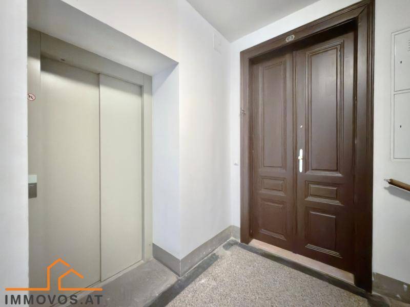 Heller Hausflur mit Aufzug und einer großen, dunklen Eingangstür zur Wohnung.