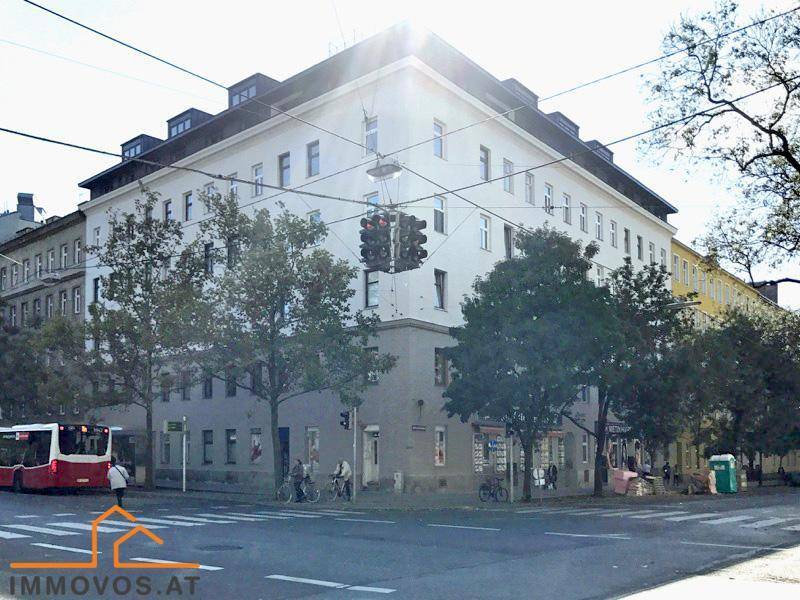 Historisches Eckgebäude in urbaner Umgebung mit vielen Fenstern und Bäumen.