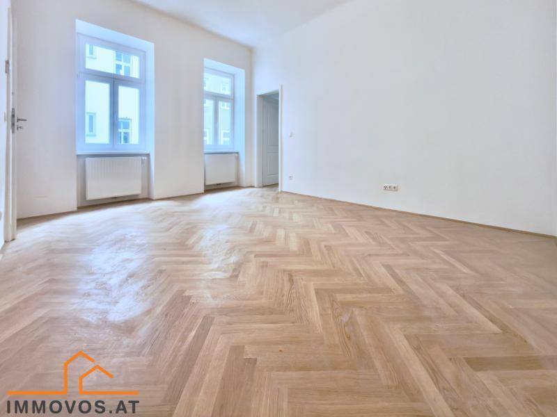 Helles, unmöbliertes Zimmer mit klassischem Fischgrätparkett und zwei hohen Fenstern.