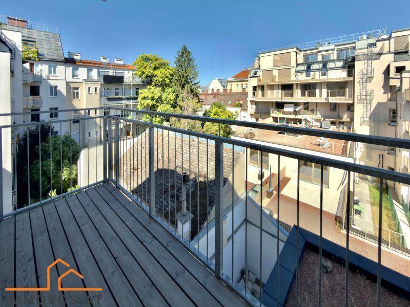 Balkon mit Holzbelag und Metallgeländer, bietet Blick auf die umliegenden Gebäude und Grünflächen.