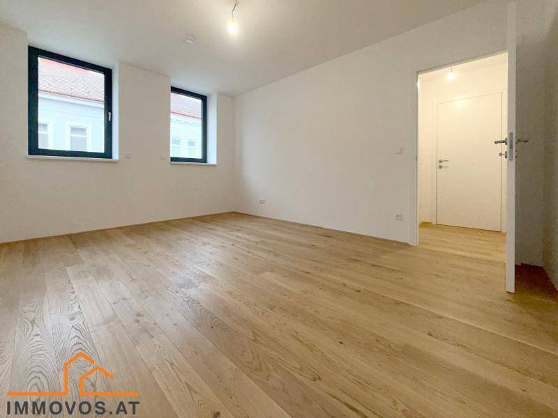 Leeres Schlafzimmer mit hellem Holzboden und zwei Fenstern, bietet viel Tageslicht.