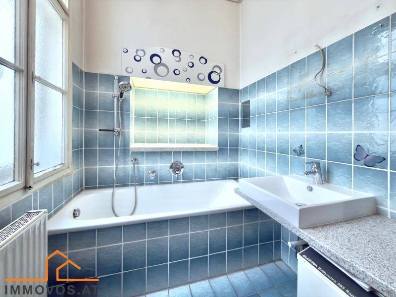 Funktionales Badezimmer mit blauen Fliesen, Badewanne, Waschbecken und Fenster.